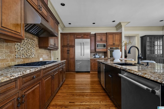 kitchen with appliances with stainless steel finishes, light stone counters, wood finished floors, under cabinet range hood, and a sink