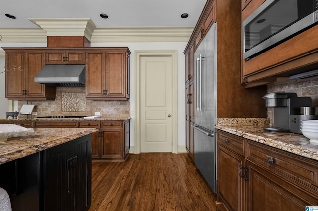 kitchen with appliances with stainless steel finishes, dark wood-type flooring, under cabinet range hood, and light stone countertops