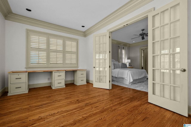 unfurnished bedroom with baseboards, wood finished floors, crown molding, french doors, and built in desk