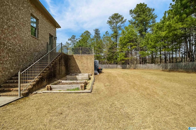 view of yard featuring a vegetable garden, fence, and stairway