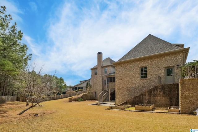 back of property featuring a chimney, stairs, fence, and a yard