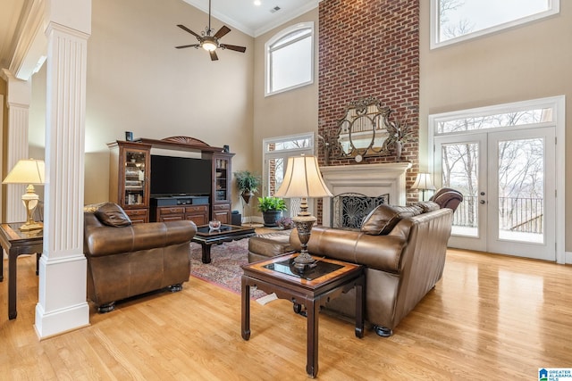 living area with a large fireplace, decorative columns, light wood-style flooring, crown molding, and french doors