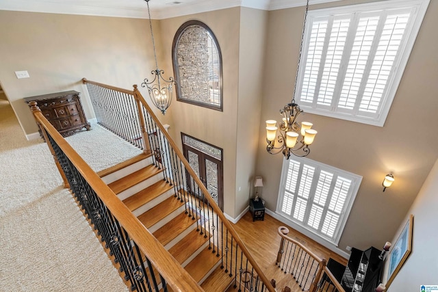 staircase featuring crown molding, baseboards, a towering ceiling, and an inviting chandelier