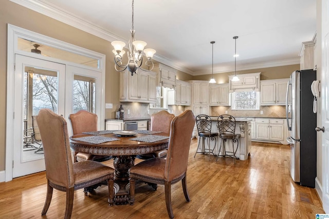 dining area with ornamental molding, a notable chandelier, and light wood-style flooring