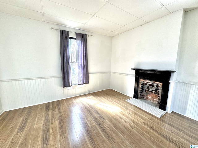 unfurnished living room with a paneled ceiling, a wainscoted wall, a fireplace, and wood finished floors