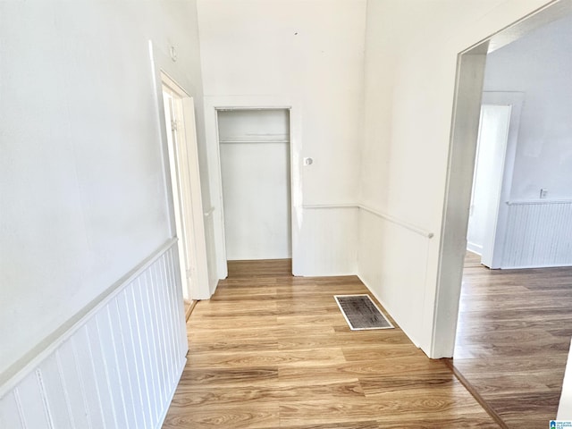 hall with a wainscoted wall, visible vents, and light wood-style flooring