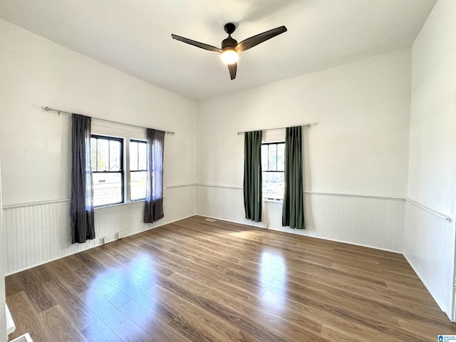 spare room with a ceiling fan, wood finished floors, and wainscoting