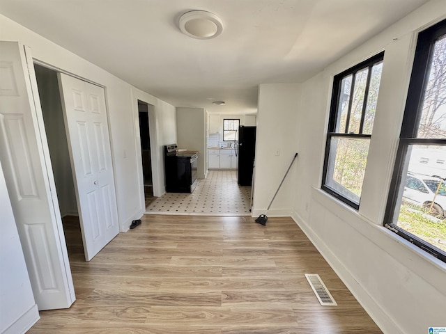 hall with baseboards, light wood-style flooring, visible vents, and a healthy amount of sunlight