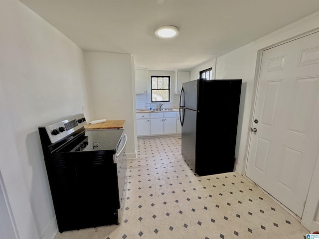 kitchen featuring a sink, white cabinets, electric stove, freestanding refrigerator, and light floors