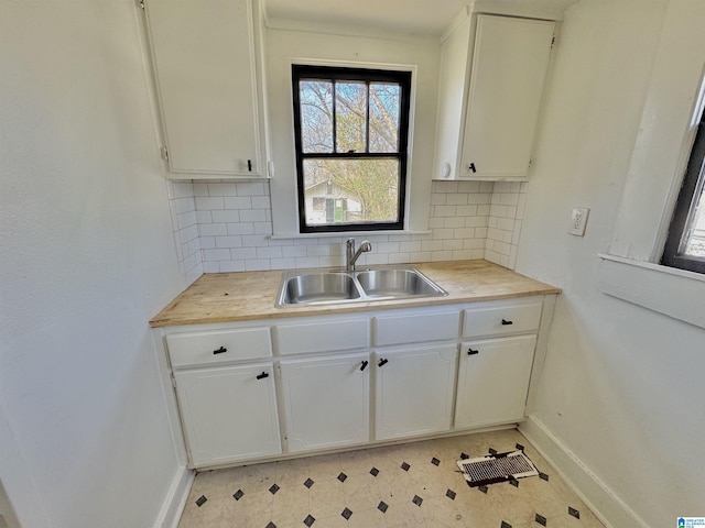 kitchen with a sink, white cabinetry, light countertops, light floors, and tasteful backsplash