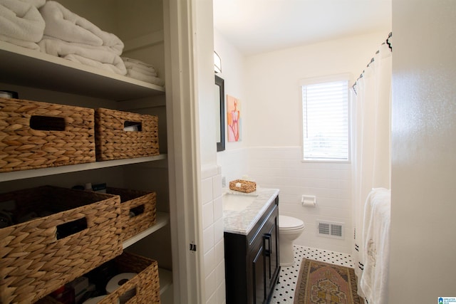 full bath featuring tile walls, visible vents, toilet, wainscoting, and vanity