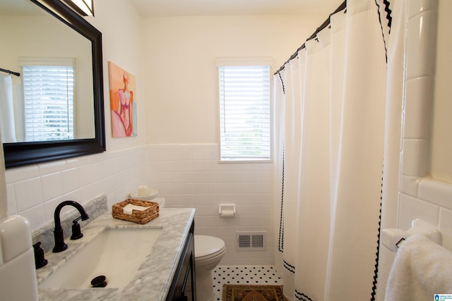 full bathroom featuring visible vents, wainscoting, toilet, vanity, and tile walls