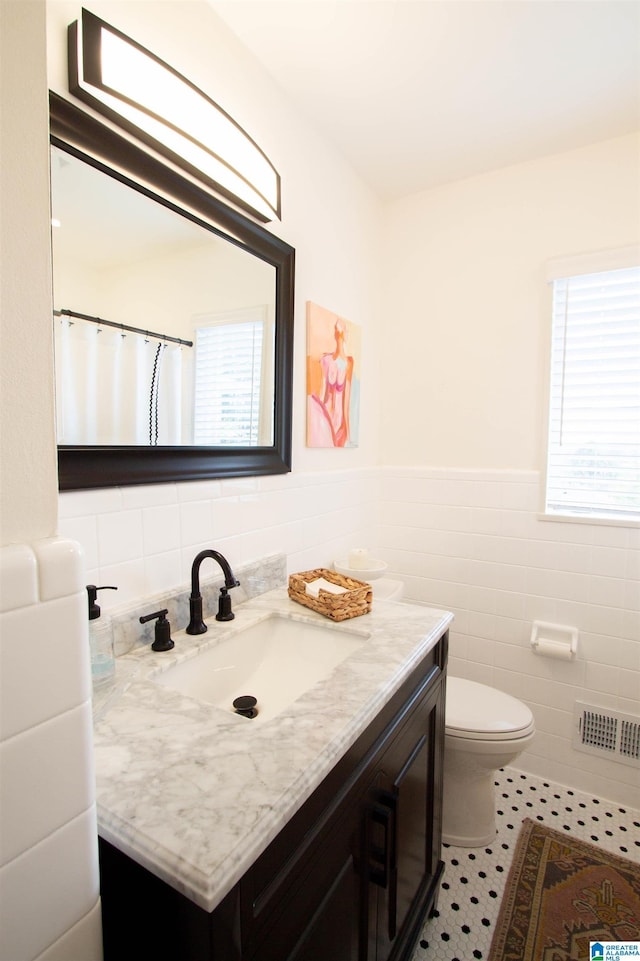 bathroom featuring visible vents, toilet, tile patterned flooring, vanity, and tile walls