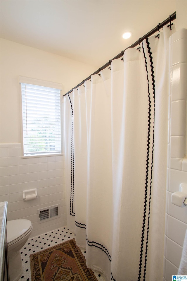 bathroom with visible vents, toilet, a shower with curtain, tile patterned flooring, and tile walls