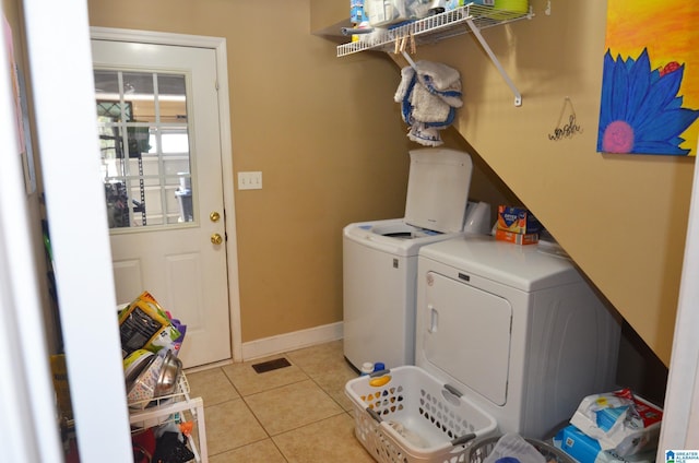 clothes washing area featuring laundry area, light tile patterned flooring, baseboards, and washing machine and clothes dryer