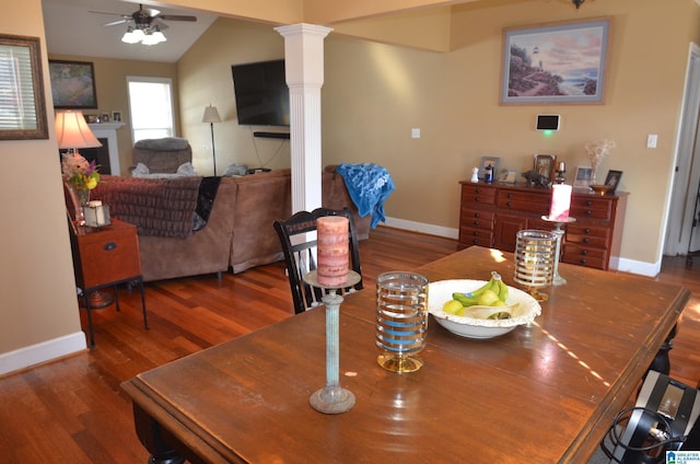 dining area featuring baseboards, a ceiling fan, wood finished floors, vaulted ceiling, and ornate columns