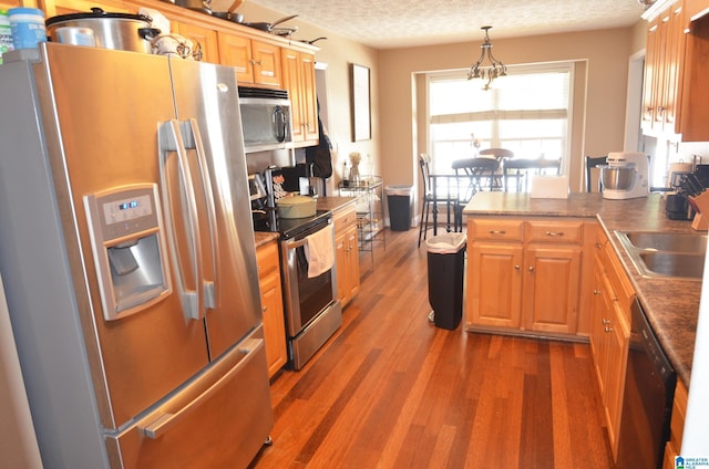 kitchen featuring stainless steel appliances, a sink, a textured ceiling, wood finished floors, and a peninsula