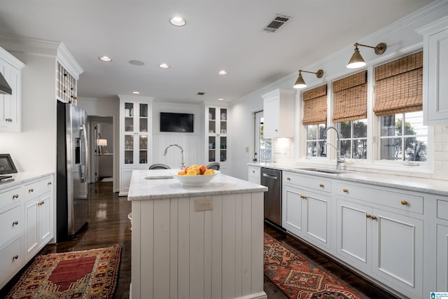 kitchen featuring crown molding, a center island with sink, appliances with stainless steel finishes, white cabinetry, and a sink