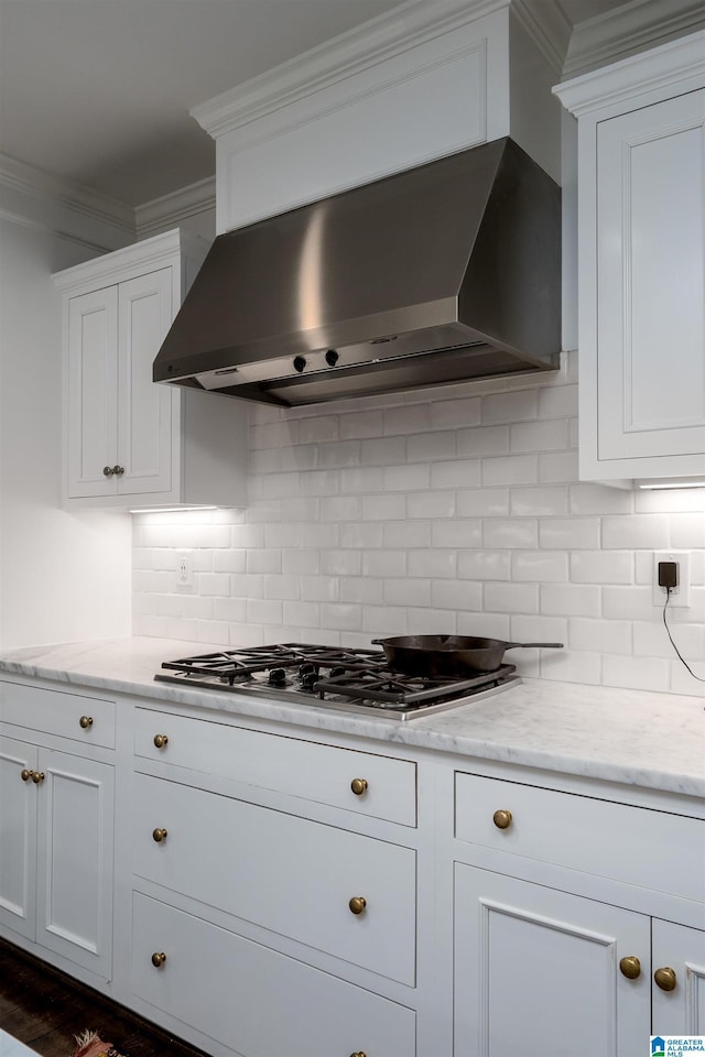 kitchen featuring wall chimney range hood, stainless steel gas cooktop, white cabinets, and ornamental molding