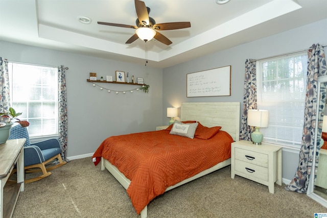 carpeted bedroom with a ceiling fan, a raised ceiling, and baseboards