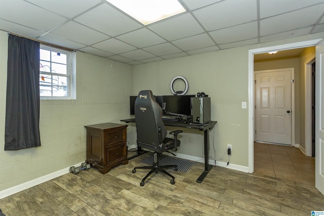 home office featuring concrete block wall, a paneled ceiling, and wood finished floors