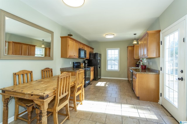 kitchen featuring light tile patterned floors, a sink, baseboards, brown cabinets, and black appliances