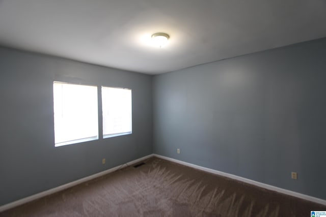 spare room featuring baseboards, visible vents, and dark colored carpet