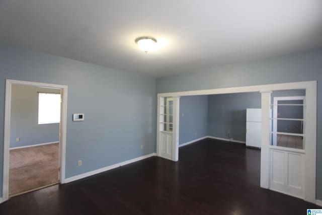 empty room featuring ornate columns, wood finished floors, and baseboards