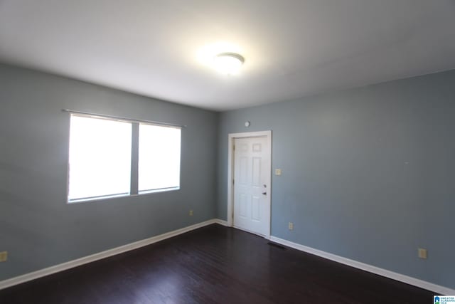 spare room with dark wood-type flooring, visible vents, and baseboards