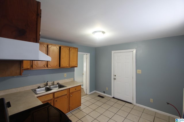 kitchen with light countertops, brown cabinetry, light tile patterned flooring, a sink, and baseboards