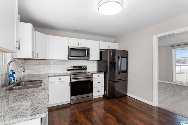 kitchen featuring white cabinets, appliances with stainless steel finishes, light stone counters, a sink, and backsplash