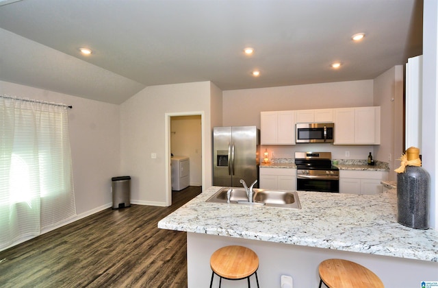 kitchen with stainless steel appliances, a peninsula, a sink, dark wood finished floors, and washer / dryer