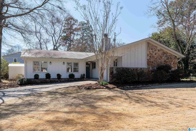 view of front of property featuring driveway, stone siding, and fence