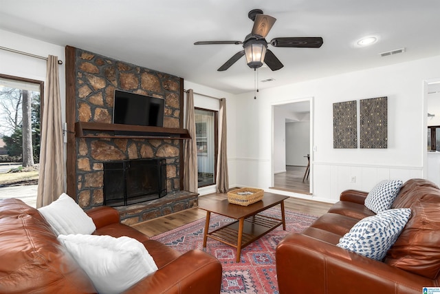 living area featuring ceiling fan, visible vents, a fireplace, and wood finished floors