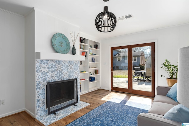 living area with built in shelves, a fireplace, wood finished floors, visible vents, and baseboards