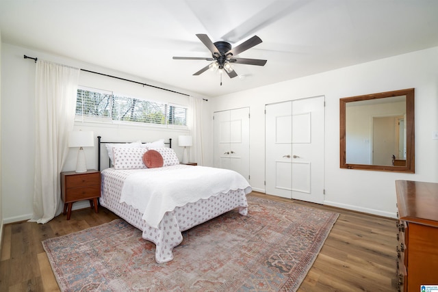 bedroom with a ceiling fan, baseboards, multiple closets, and wood finished floors