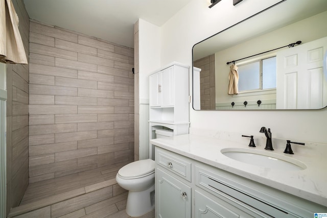 bathroom featuring vanity, a tile shower, and toilet