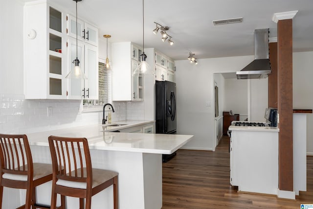 kitchen featuring a breakfast bar area, visible vents, a sink, wall chimney range hood, and black fridge