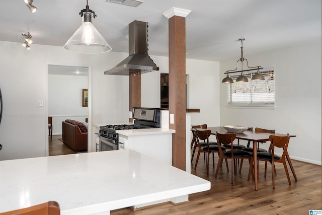 kitchen featuring visible vents, island range hood, wood finished floors, light countertops, and stainless steel range with gas cooktop