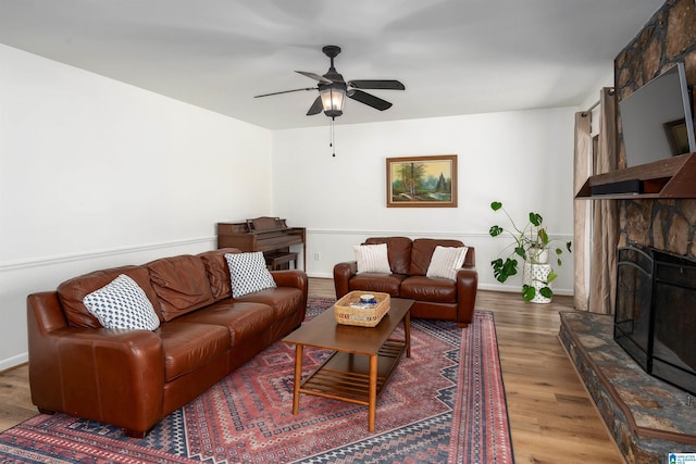 living area featuring ceiling fan, a fireplace, baseboards, and wood finished floors