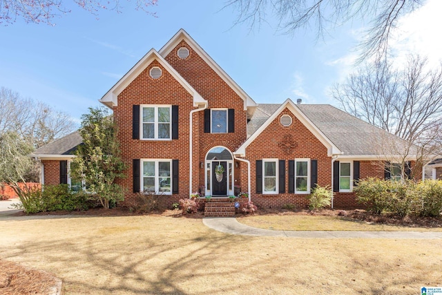 traditional-style house featuring brick siding, a shingled roof, and a front yard