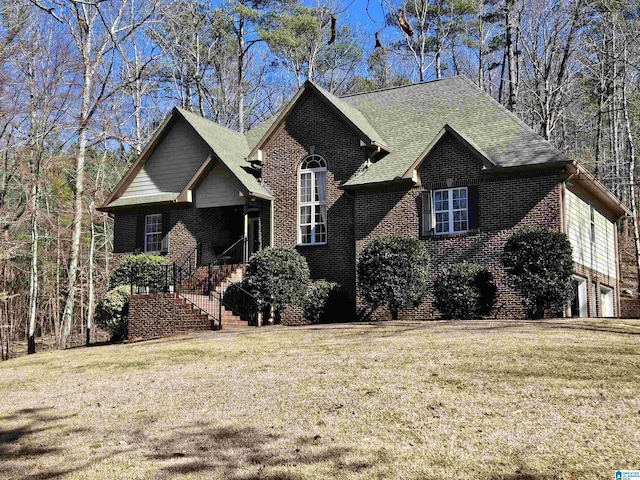 view of front of house featuring a front lawn, brick siding, and roof with shingles