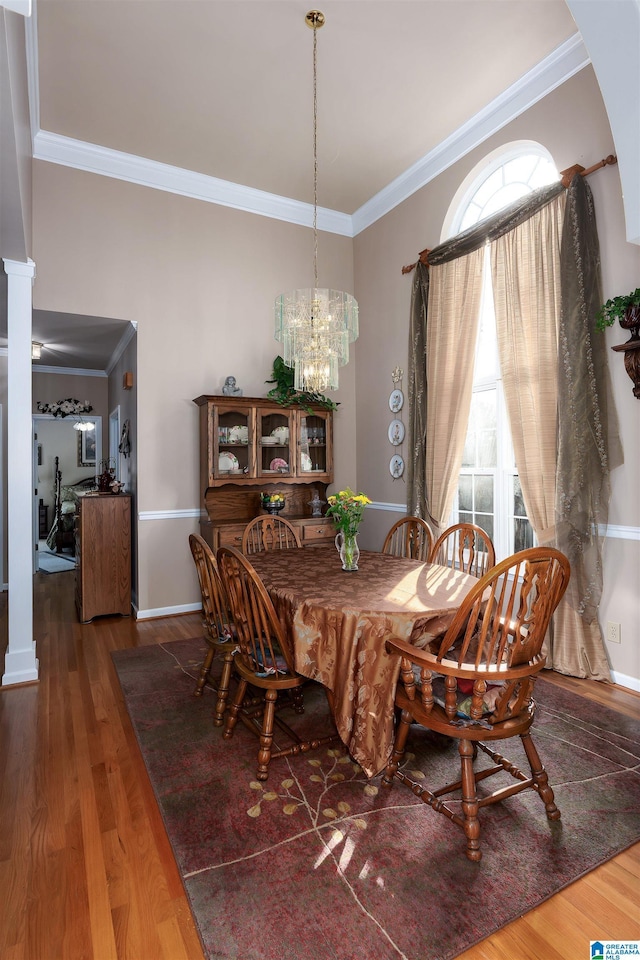 dining space featuring wood finished floors, baseboards, decorative columns, crown molding, and a chandelier