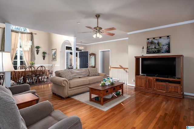 living area featuring a ceiling fan, baseboards, wood finished floors, arched walkways, and ornamental molding