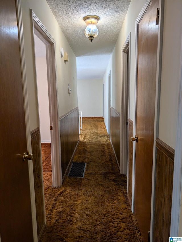 hall featuring wainscoting, visible vents, dark carpet, and a textured ceiling