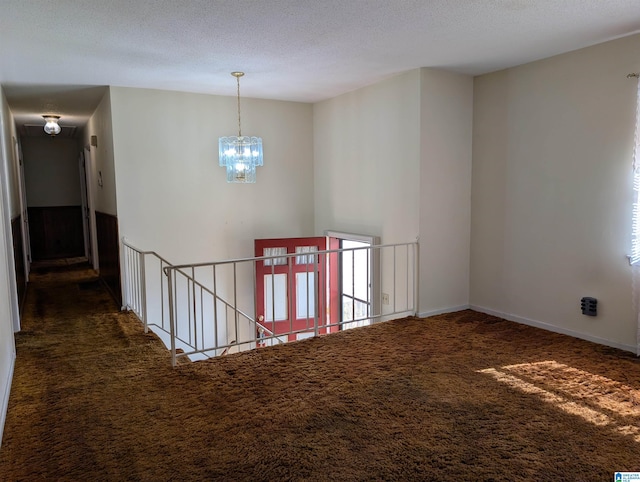 hallway with an inviting chandelier, a textured ceiling, baseboards, and carpet flooring