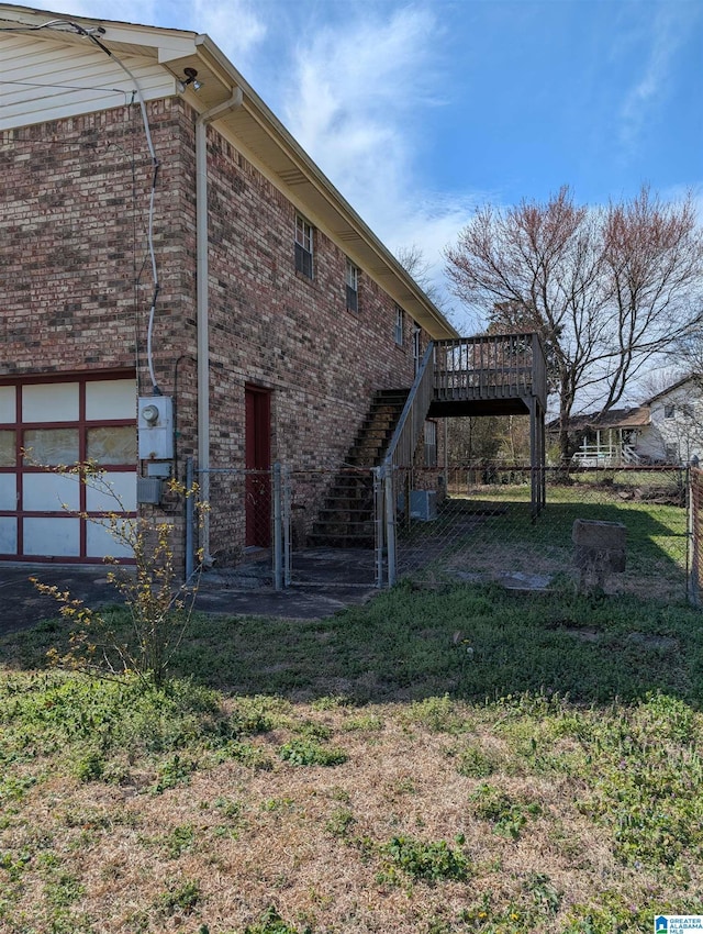 view of home's exterior featuring brick siding, fence, stairway, and a wooden deck