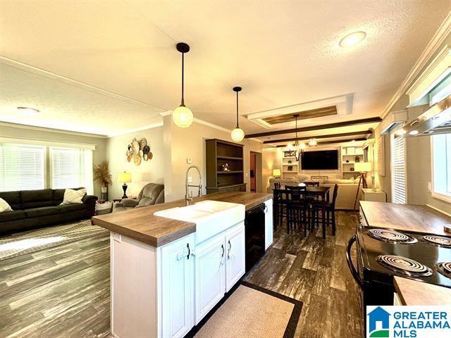 kitchen with a raised ceiling, ornamental molding, open floor plan, black appliances, and a sink