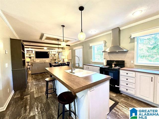 kitchen featuring dark wood finished floors, white cabinets, a sink, wall chimney range hood, and black / electric stove