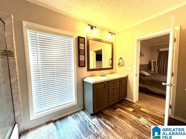 full bathroom featuring a textured ceiling, a sink, wood finished floors, double vanity, and ensuite bath